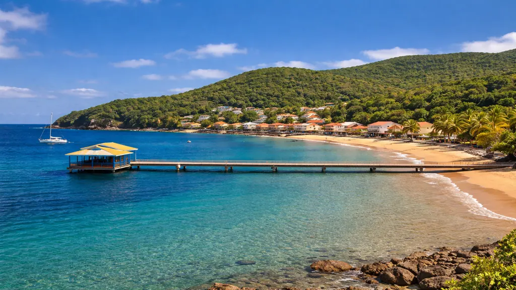 Vue panoramique de Deshaies en Guadeloupe avec plage tropicale, eau turquoise, ponton sur la baie et village bordé de végétation luxuriante
