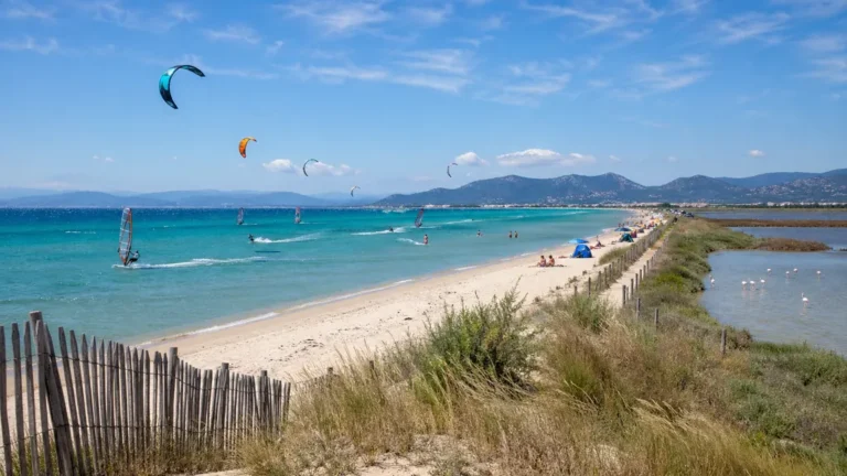 Plage de l’Almanarre à Hyères avec mer turquoise, kitesurf et salins de Pesquiers en arrière-plan.