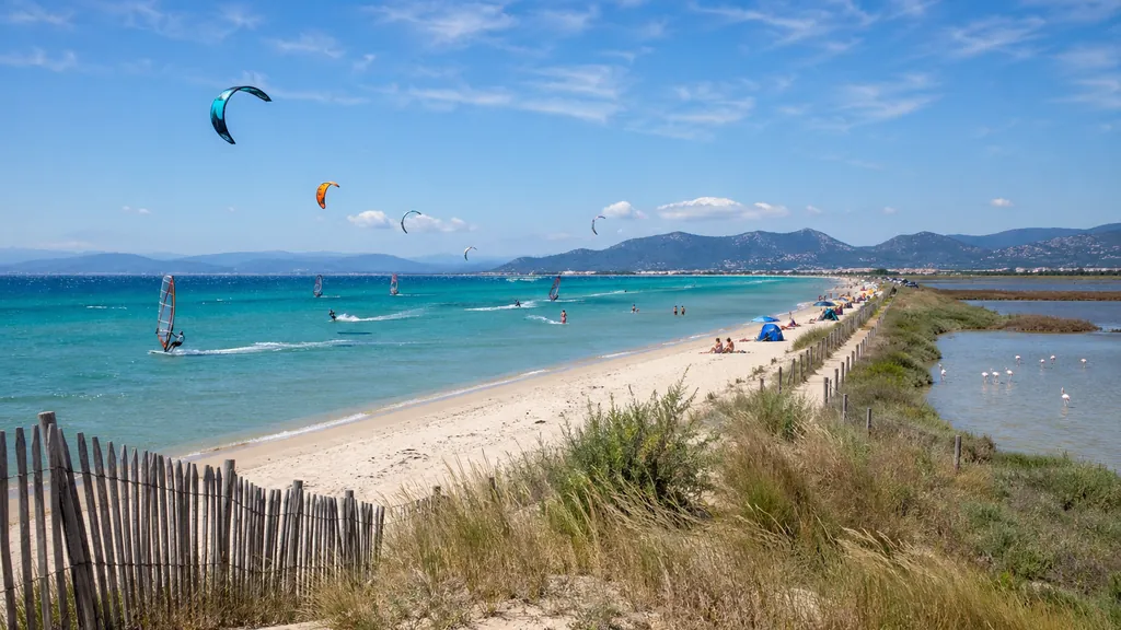 Plage de l’Almanarre à Hyères avec mer turquoise, kitesurf et salins de Pesquiers en arrière-plan.