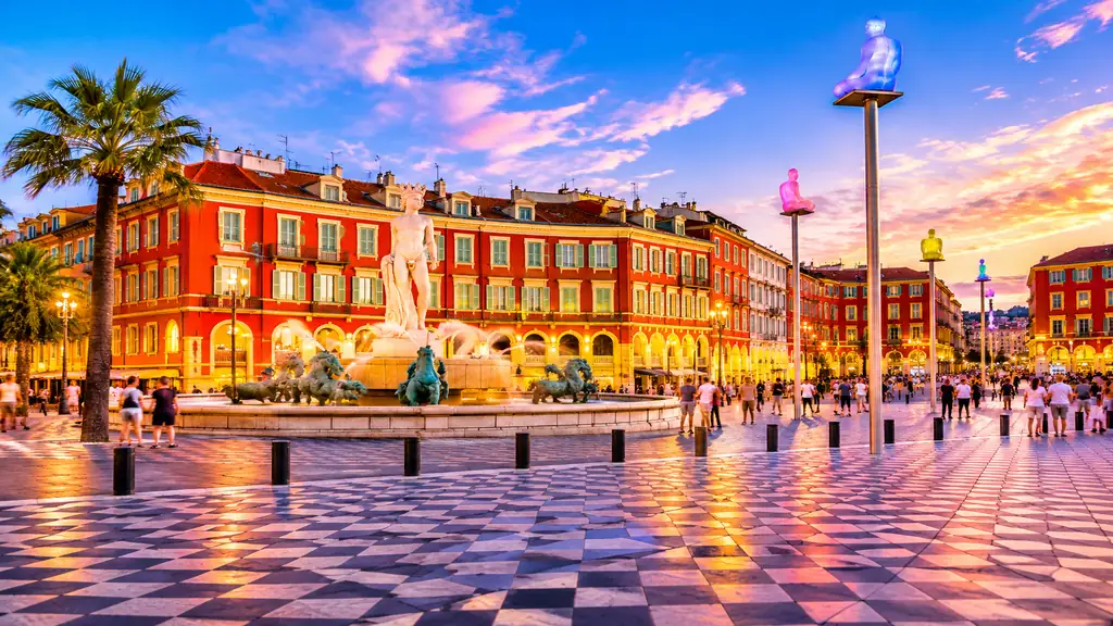 Vue réaliste de la Place Masséna à Nice avec fontaine du Soleil, façades rouges, pavés en damier et sculptures lumineuses.