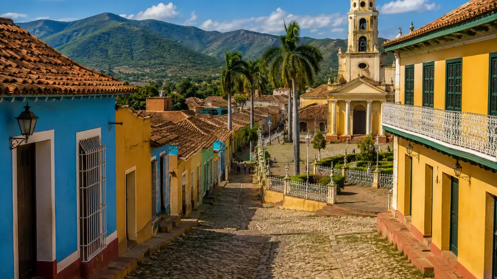 Rue coloniale colorée de Trinidad à Cuba avec façades pastel, clocher historique et montagnes en arrière-plan.