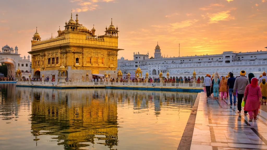 Temple d’Or d’Amritsar au coucher du soleil avec reflet dans le bassin sacré et pèlerins autour du sanctuaire