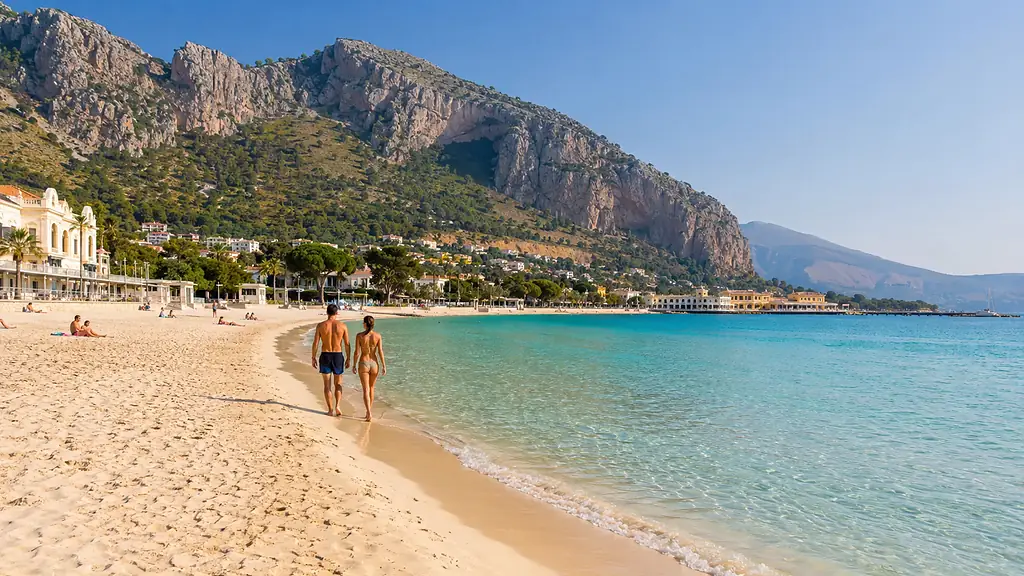 Plage de Mondello à Palerme avec sable clair, eau turquoise, promeneurs et montagnes en arrière-plan