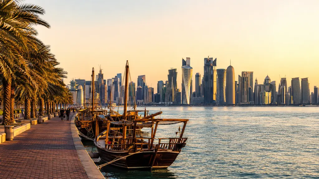Vue de Doha au Qatar avec skyline moderne, corniche, palmiers et bateaux traditionnels au coucher du soleil