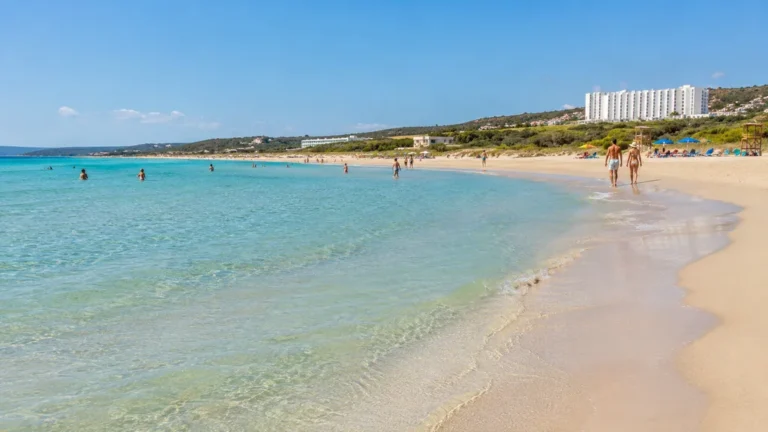 Plage de Son Bou à Minorque avec eau turquoise peu profonde, grande étendue de sable et vacanciers en bord de mer.