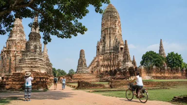 Visiteurs découvrant les temples anciens du parc historique d’Ayutthaya avec ruines de briques, stupas et vélo sous le soleil thaïlandais.
