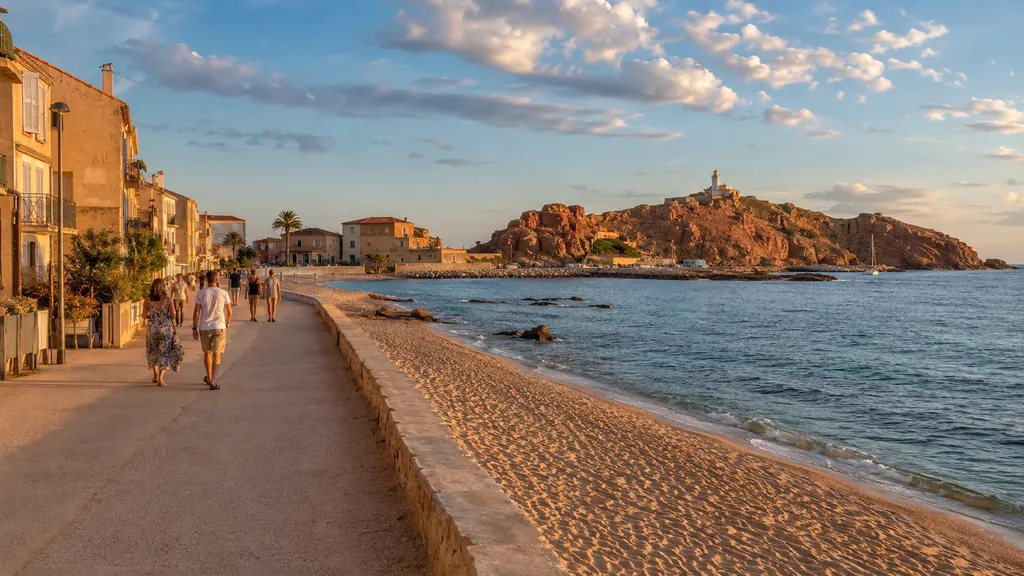 Promenade de L’Île-Rousse en Corse avec plage, mer turquoise et phare de la Pietra au coucher du soleil
