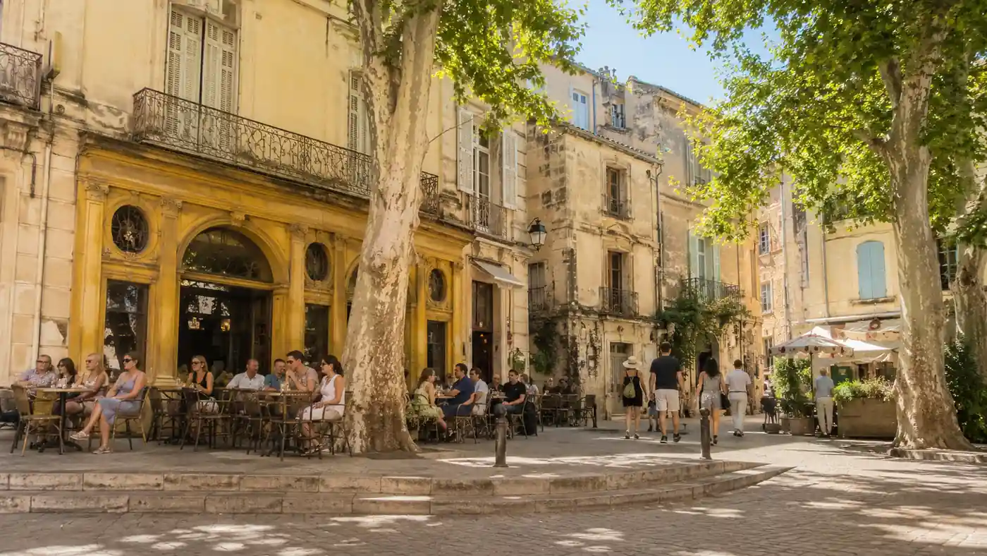 Terrasses animées et façades historiques de la place du Forum à Arles sous les platanes