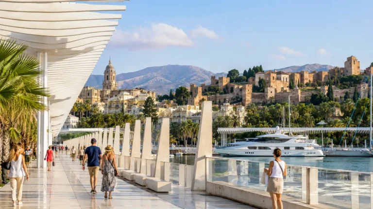 Promeneurs à Malaga sur Muelle Uno avec vue sur l’Alcazaba, la cathédrale, le port et les montagnes en arrière-plan.